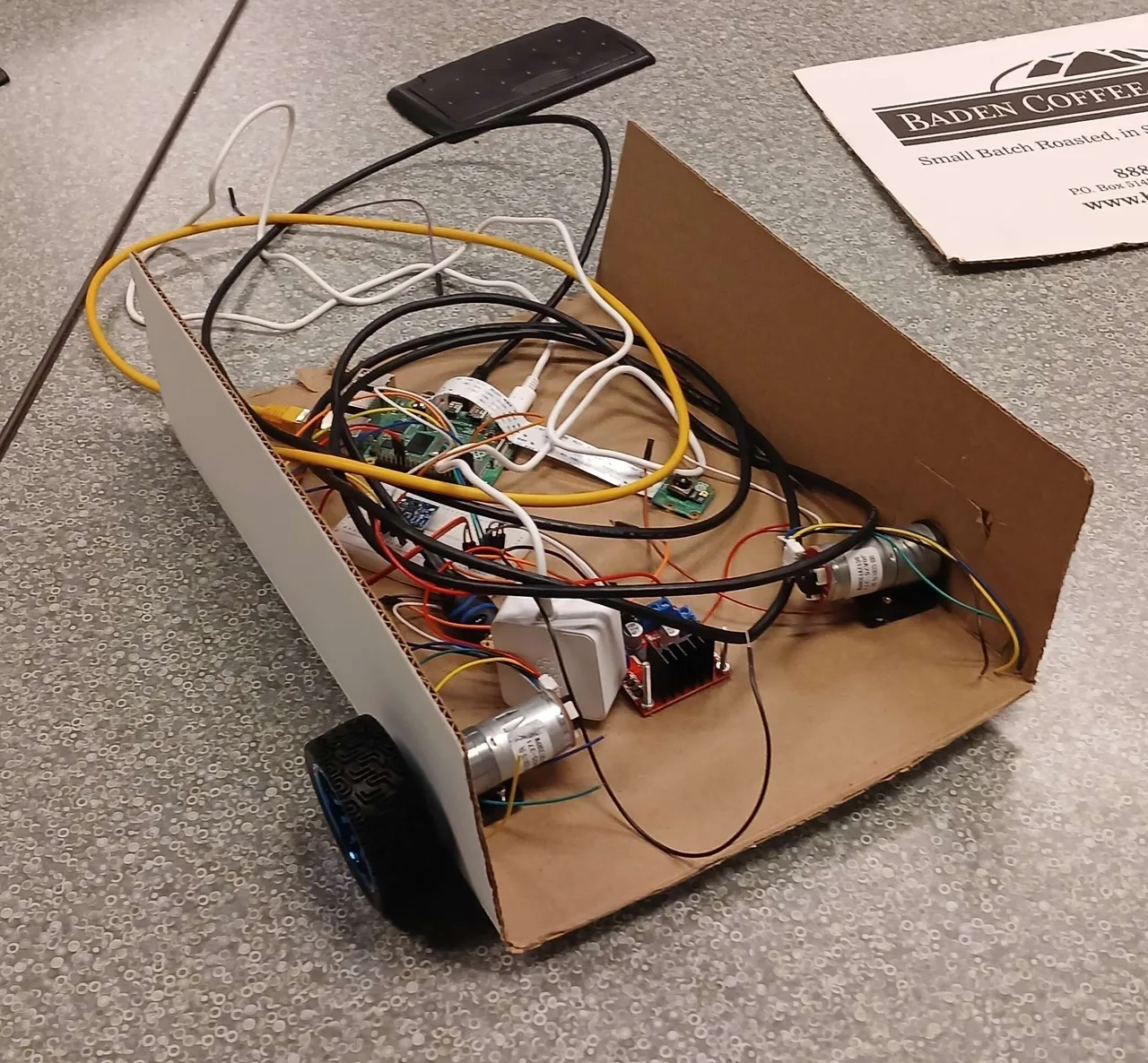 Carboard, with a Raspberry Pi, camera, motor driver and wheels on a cardboard chassis