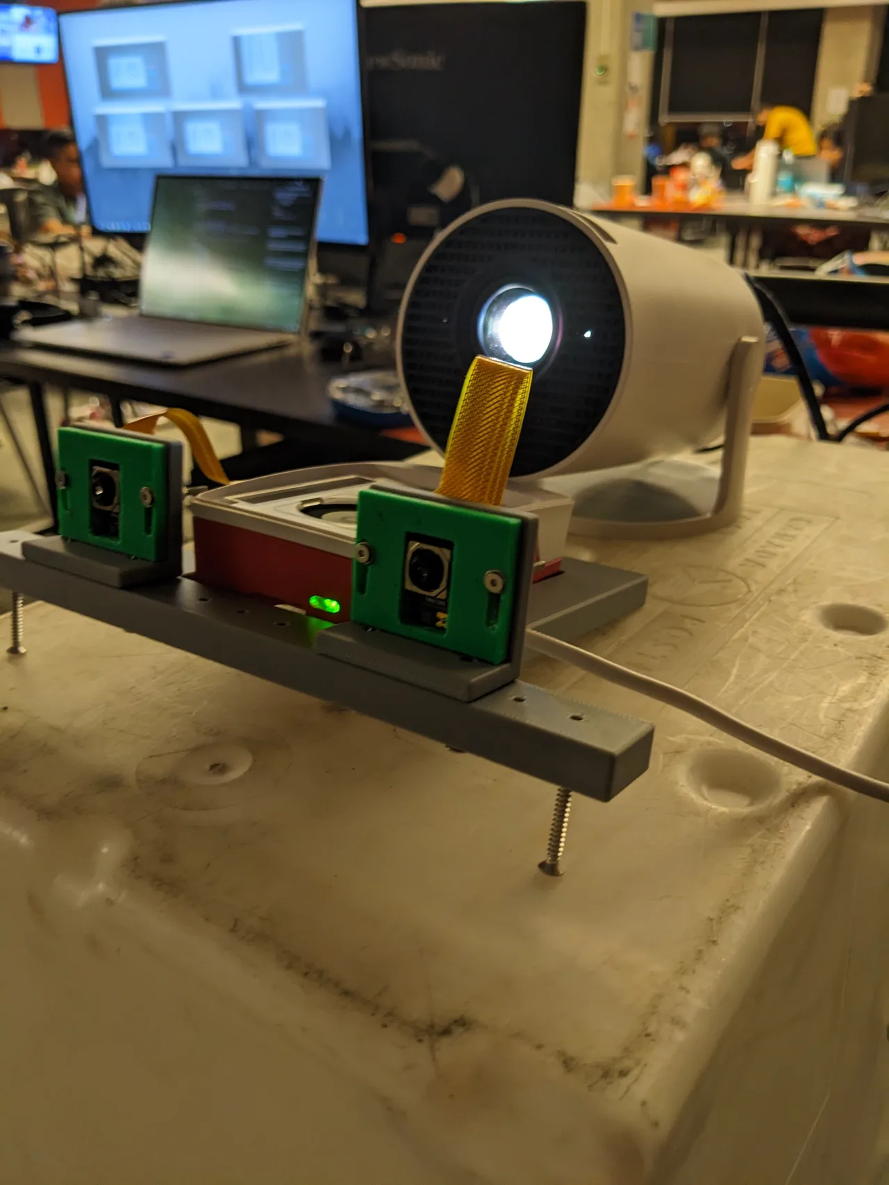 Two Pi cameras in front of a Raspberry Pi case and a projector on the hackathon workbench