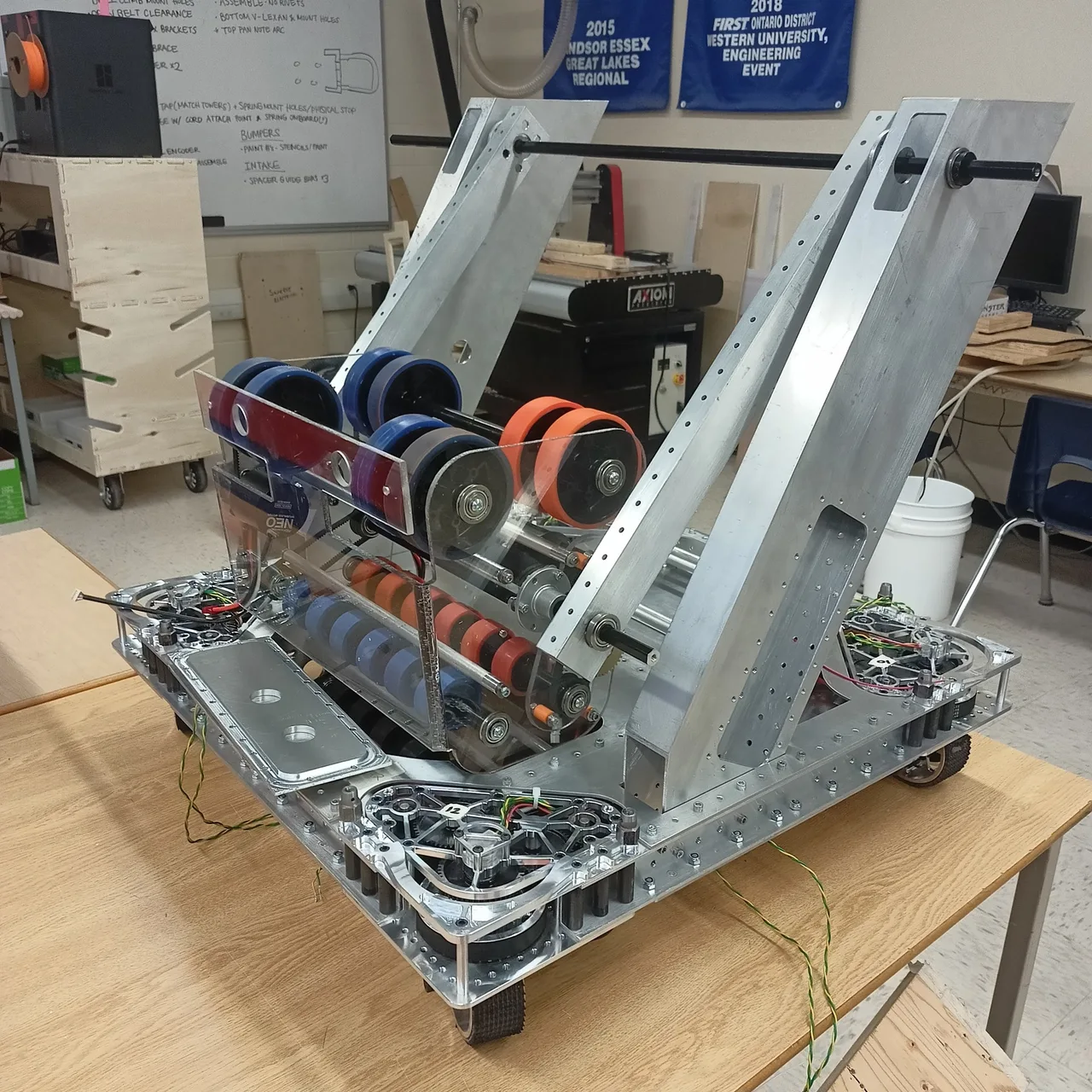 Robot chassis and roller assembly on a workbench, with belts, motors and aluminum side plates visible